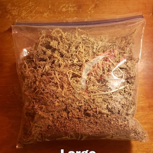 May include: A clear plastic bag filled with dried, brown moss. The bag is sealed with a blue zipper closure. The word "Large" is printed in white at the bottom of the bag. The moss appears to be a natural material.
