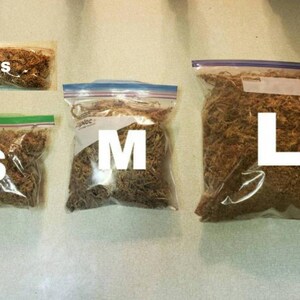 May include: Four clear plastic bags filled with brown dried moss, labeled XS, S, M, and L in large white letters. The bags are sealed with a zip closure, and the moss appears to be a natural product, likely for crafting or decorative purposes.