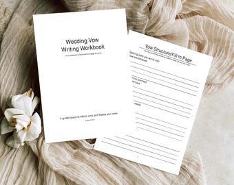 May include: Two white workbooks titled "Wedding Vow Writing Workbook" and "Vow Structure/Fill In Page" are displayed on a beige fabric surface. The first workbook has text that reads "A guided space to reflect, write, and finalize your vows." A white flower is in the lower left corner.