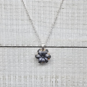 May include: A silver chain necklace with a black bullet pendant. The bullet is shaped like a flower with five petals.