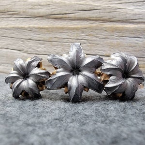 Peut inclure: Trois douilles de balle de couleur argentée avec un motif en forme d'étoile. Les douilles sont disposées en rangée sur une surface grise.