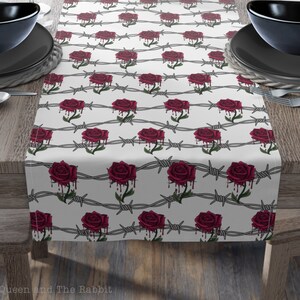 May include: White table runner with a repeating pattern of red roses and barbed wire. The roses are dripping with blood.