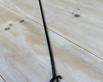 May include: A black, hand-forged fireplace poker with a U-shaped end and a twisted handle. The poker has a curved hook at the bottom. The tool is designed for tending to a fire.