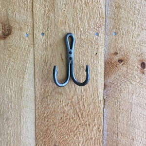 May include: A silver double hook with two points, mounted on a wooden wall.