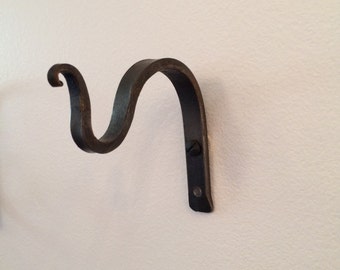 May include: A black metal wall-mounted hook with a decorative scroll design. The hook is attached to the wall with two screws.