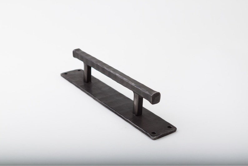 May include: A black metal door pull handle with a rectangular backplate. The handle is textured and has a squared-off end.