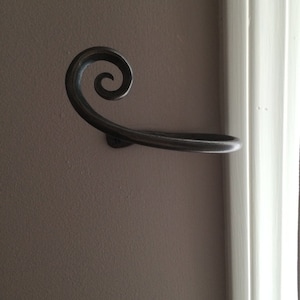May include: A black metal towel rack with a decorative scroll design. The rack is mounted to a wall.
