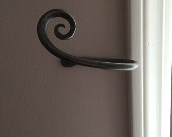 May include: A black metal towel rack with a decorative scroll design. The rack is mounted to a wall.