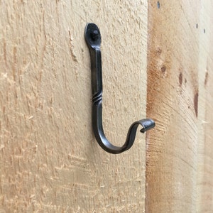 May include: A black metal hook with a decorative twist design is mounted on a light wood surface.