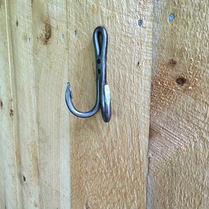 May include: A black metal hook with a curved design, mounted on a wooden surface.