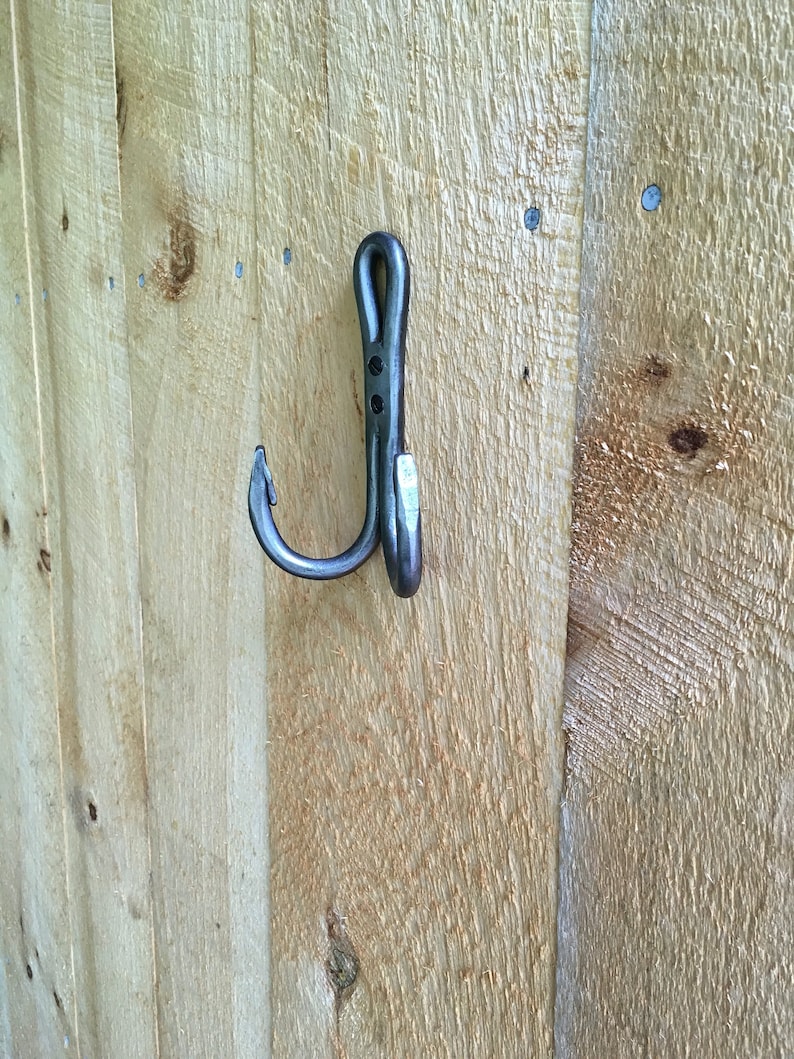 May include: A black metal hook with a curved design, mounted on a wooden surface.