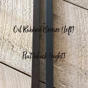 May include: Two metal rods, one with an oil rubbed bronze finish and the other with a flat black finish. The text "Oil Rubbed Bronze (left)" and "Flat Black (right)" is written on the wood surface behind the rods.