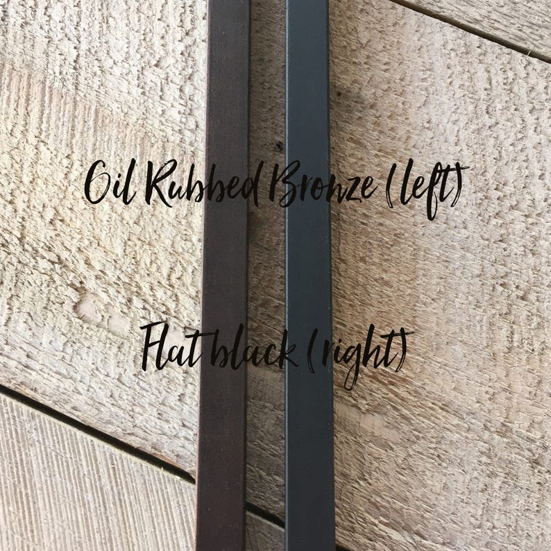 May include: Two metal rods, one with an oil rubbed bronze finish and the other with a flat black finish. The text "Oil Rubbed Bronze (left)" and "Flat Black (right)" is written on the wood surface behind the rods.