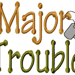 May include: Embroidered design with the text "Major Trouble" in gold and green lettering. Two gray dog tags are attached to the word "Major".