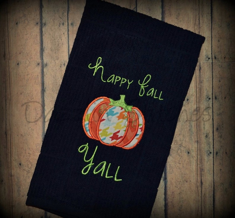 May include: A dark blue kitchen towel with the text "Happy Fall Y'all" embroidered in green. A colourful pumpkin with a green stem is embroidered in the centre of the towel.
