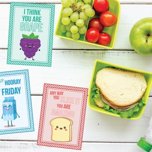 Peut inclure: Vue de dessus sur une surface en bois blanc avec un th&egrave;me de d&eacute;jeuner. Trois cartes illustr&eacute;es avec le texte : "I THINK YOU ARE GRAPE", "SIP SIP HOORAY IT'S FRIDAY" et "ANY WAY YOU SLICE IT YOU ARE AMAZING". Il y a aussi des conteneurs de raisins, de tomates et un sandwich.