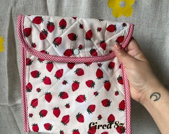May include: A quilted white pouch with a repeating pattern of red strawberries. The pouch has a red and white gingham trim and a snap closure. The text "Circa 85" is printed on the lower right corner.