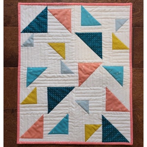May include: A white quilt with a pink border. The quilt is made up of a patchwork of triangles in various colors, including teal, blue, yellow, and pink.