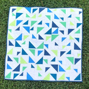 May include: A white quilt with a geometric pattern of blue, green, and yellow triangles.