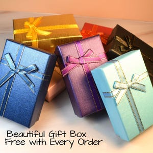 May include: A collection of colorful gift boxes, including blue, gold, purple, and black, each adorned with a matching ribbon. The boxes are arranged in a visually appealing display, with the text "Beautiful Gift Box Free with Every Order" at the bottom.