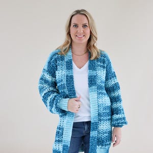 Peut inclure: Un cardigan ouvert à manches longues avec un motif crocheté texturé et varié dans des tons bleu sarcelle, marine et bleu clair. Le vêtement présente une bordure côtelée le long de l'ouverture avant et des poignets, avec une coupe ample.