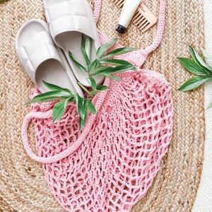 May include: A pink crochet mesh bag with two grey quilted sliders on a woven jute rug.