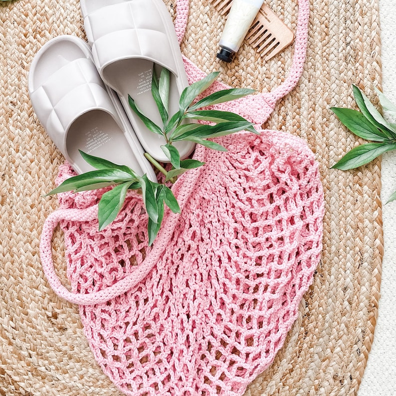 May include: A pink crochet mesh bag with two grey quilted sliders on a woven jute rug.