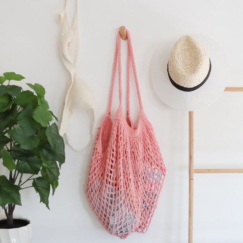 May include: A pink crocheted mesh bag hanging on a hook. The bag is empty and has a wide, open top.