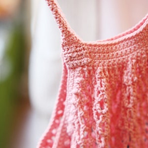 May include: A close-up of a pink crocheted top with a delicate, lacy design. The top is made with a soft, lightweight yarn and has a relaxed, flowy fit.