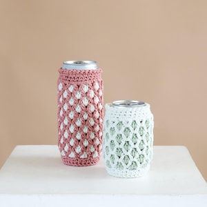 May include: Two crochet can sleeves, one tall dusty rose sleeve with white textured accents and one shorter white sleeve with light green textured accents, each fitted around a metallic beverage can to provide a decorative exterior layer.
