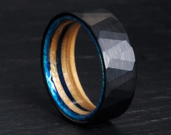 May include: A black faceted ring with a blue and wood-tone interior. The ring has a geometric design and a polished finish. The inner band features a vibrant blue resin and light wood grain.