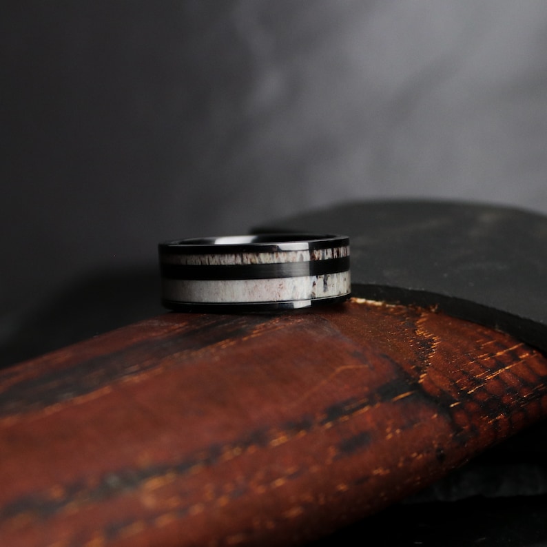 Puede incluir: Un anillo negro con una banda de material blanco y marr&oacute;n. El anillo tiene una banda exterior negra. El anillo est&aacute; sobre una superficie marr&oacute;n.