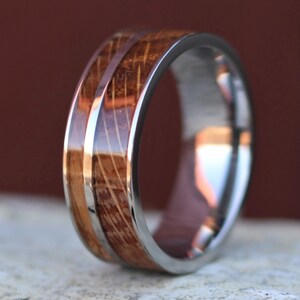 Puede incluir: Primer plano de un anillo con una banda de acero inoxidable y una incrustaci&oacute;n de madera. La madera tiene un patr&oacute;n de vetas natural y un color marr&oacute;n c&aacute;lido. El anillo est&aacute; dise&ntilde;ado con un acabado pulido, que refleja la luz.