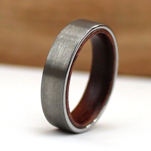 May include: A silver ring with a brushed metal surface, featuring a dark wood inner band and a thin silver edge. The ring is a simple band design, suitable for everyday wear. The ring's interior is made of wood.