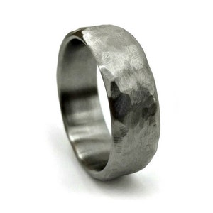 May include: A textured, silver-colored ring with a hammered finish. The ring has a rounded band and a slightly irregular surface, creating a unique, handcrafted appearance. The ring is shown against a white background.