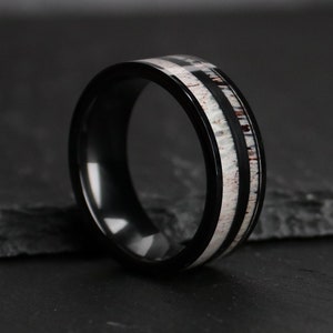Puede incluir: Un anillo negro con una incrustaci&oacute;n blanca y marr&oacute;n. El anillo tiene un acabado negro pulido y una banda ancha. La incrustaci&oacute;n presenta un patr&oacute;n geom&eacute;trico con una apariencia natural y texturizada. Un accesorio elegante.