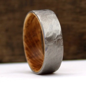May include: A close-up of a ring with a hammered, gray metal exterior and a light brown wooden interior. The ring has a band width of approximately 6 mm.
