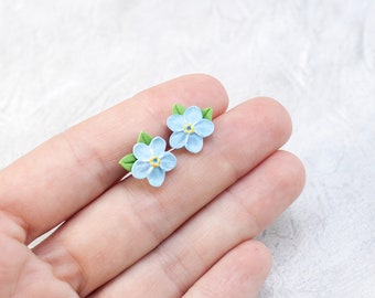 May include: A pair of blue forget-me-not flower earrings with green leaves.