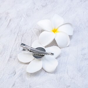May include: Two white flower hair clips with a silver clip. The flowers are made of fabric and have a yellow center.