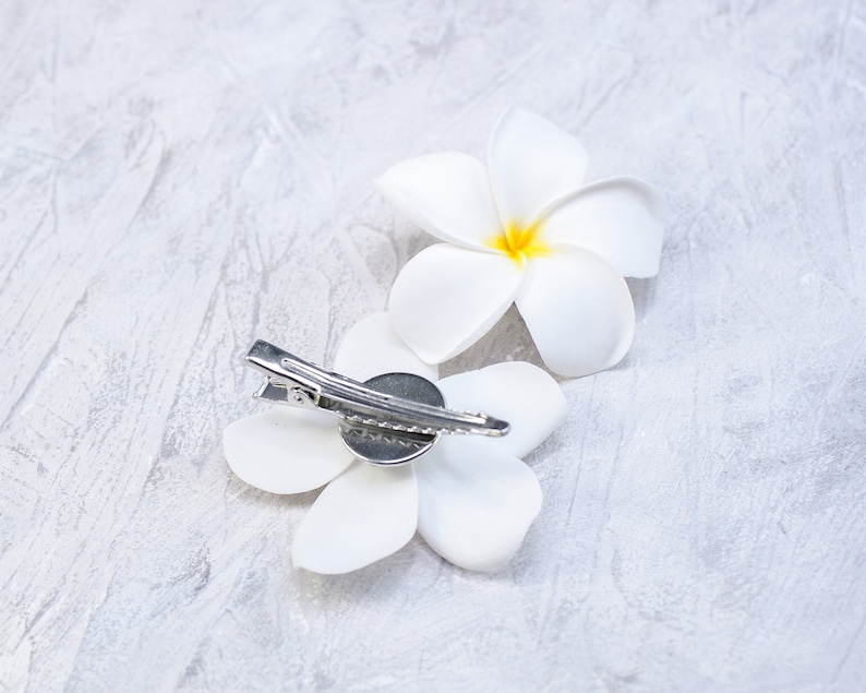May include: Two white flower hair clips with a silver clip. The flowers are made of fabric and have a yellow center.