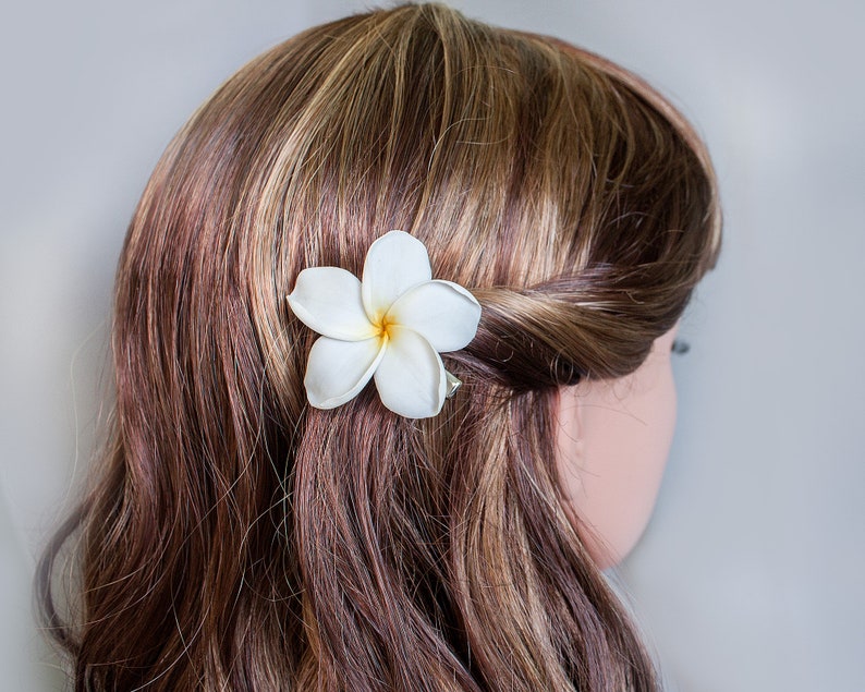 May include: A white flower hair clip with a brown and blonde hairstyle.