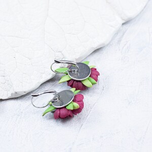 May include: A pair of earrings featuring pink flower designs with green leaves. The earrings have silver hooks.