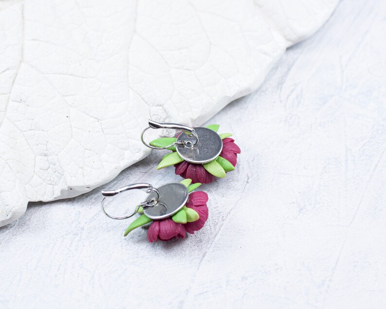 May include: A pair of earrings featuring pink flower designs with green leaves. The earrings have silver hooks.