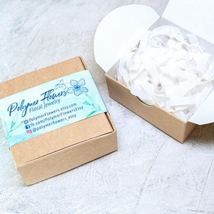 May include: A small brown cardboard box with a white and blue label that says "Polymer Flowers Floral Jewelry" and includes contact information for the shop. The box is filled with white tissue paper.