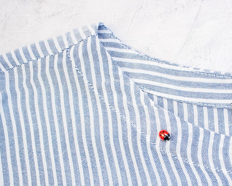 May include: A close-up of a blue and white striped fabric with a red ladybug button.