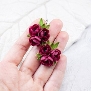May include: A pair of burgundy flower earrings with green leaves. The earrings are made of polymer clay and are handmade.