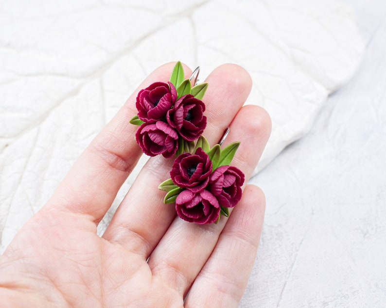 May include: A pair of burgundy flower earrings with green leaves. The earrings are made of polymer clay and are handmade.