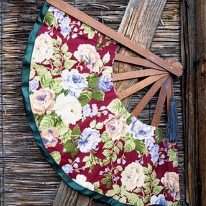 May include: A floral patterned hand fan with a wooden frame and a green ribbon trim. The fan is closed and has a tassel hanging from the end.