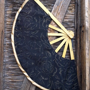 May include: A black fabric fan with a gold trim and a floral pattern. The fan is made of wood and has a handle with the word "PARIS" written on it.