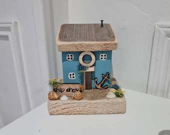 Barco a la vista. Casa de campo cosey azul junto al mar con ancla, rocas, flores y arena y un pequeño letrero estampado a mano. arte costero, regalo del día del padre